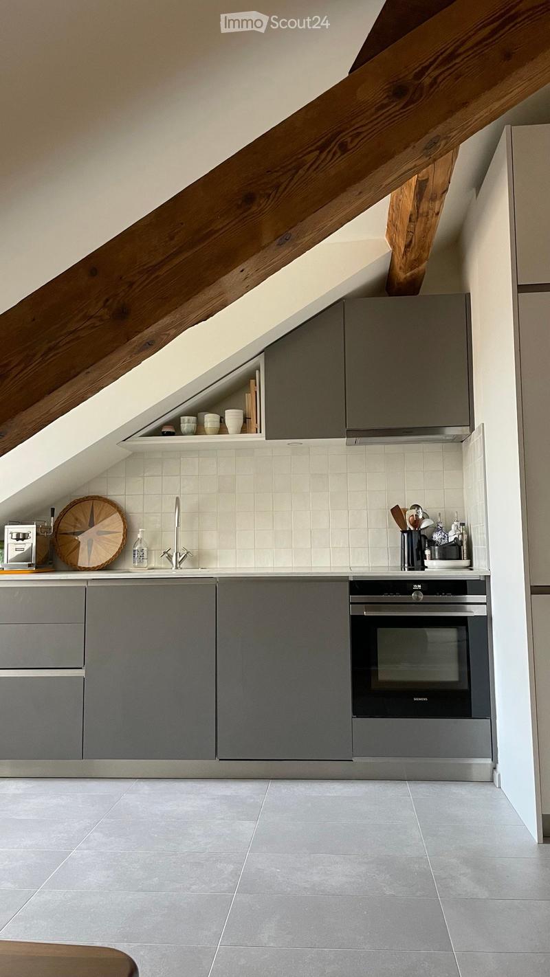 Modern kitchen with grey cabinets, white tiled backsplash, and stainless steel appliances. Features a sink, faucet, oven, and various kitchen utensils on the counter.