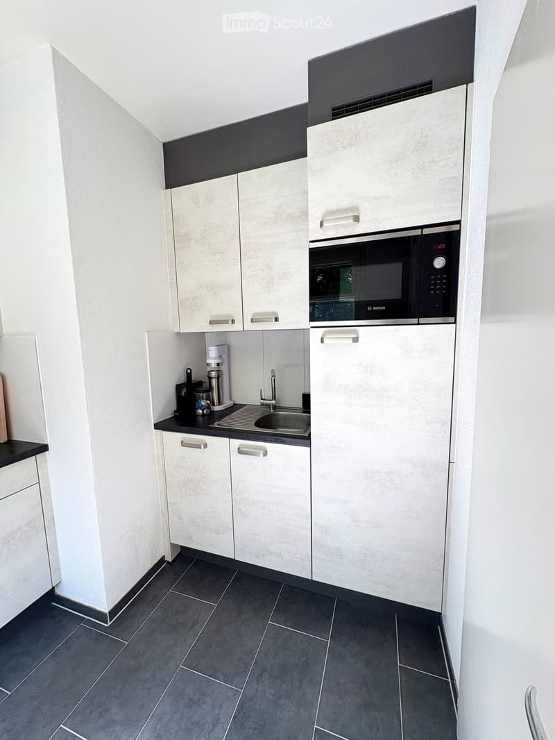 Modern kitchen with white cabinets, dark countertops, and stainless steel appliances including a microwave and sink.