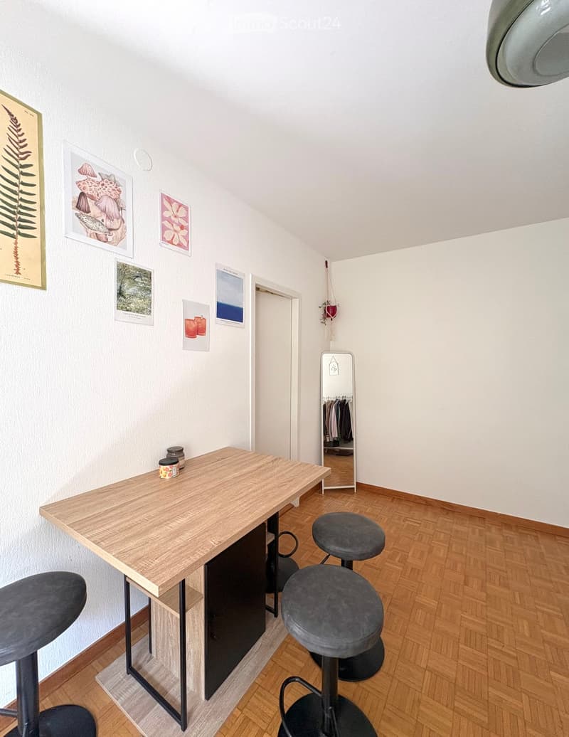 A modern, minimalist room with a wooden table, four grey stools, a mirror, and several picture frames on the wall.