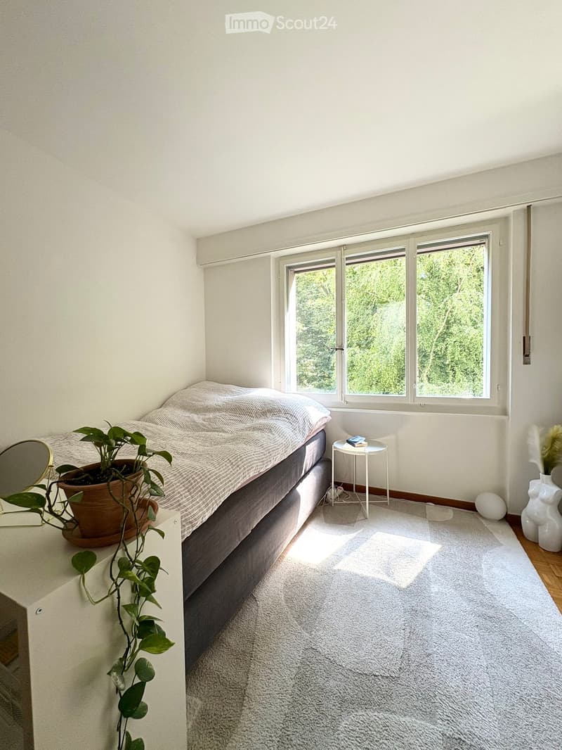 Minimalist bedroom with a bed, nightstand, mirror, small table, plant, and decorative vases.