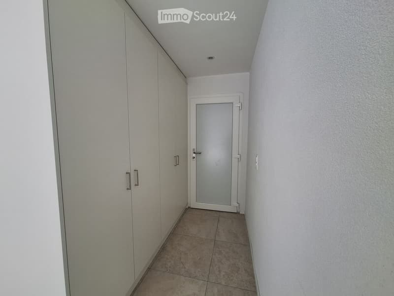 Empty hallway with tiled floor, white walls, and a closed door at the end.