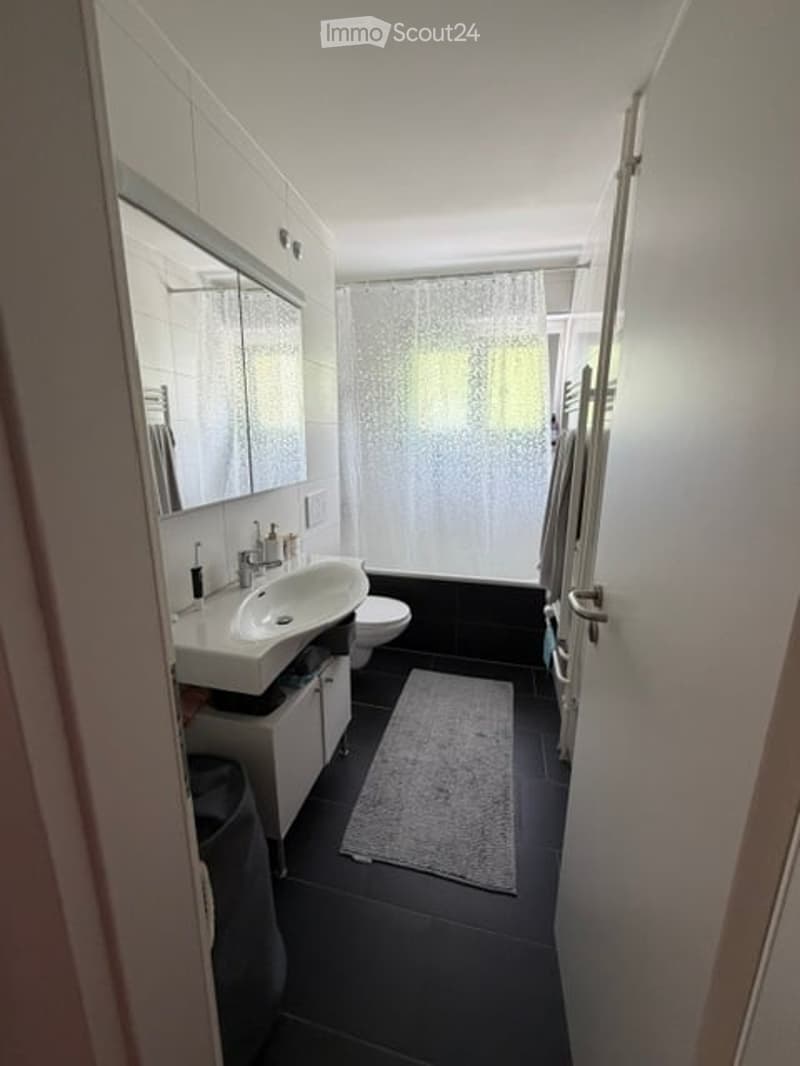 Modern bathroom with white walls, black tiled floor, white sink, toilet, mirror, and shower curtain.