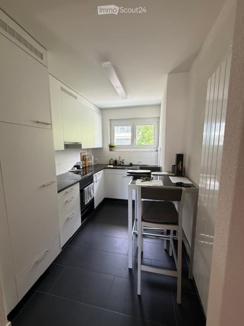 Modern kitchen with white cabinets, black tiled floor, and a small dining area with a table and chair.
