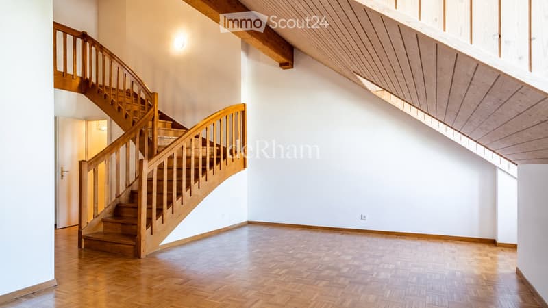 Spacious hallway with wooden staircase, polished wooden floor, white walls, and exposed wooden ceiling beams.