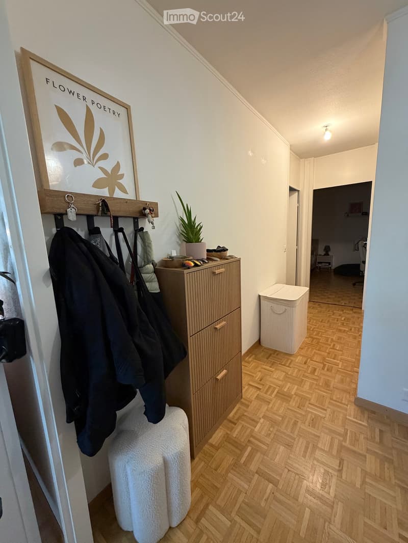 Hallway with wooden flooring, coat rack with jackets, small storage cabinet, potted plant, and a trash bin. A sign reading "FLOWER POETRY" is mounted on the wall.