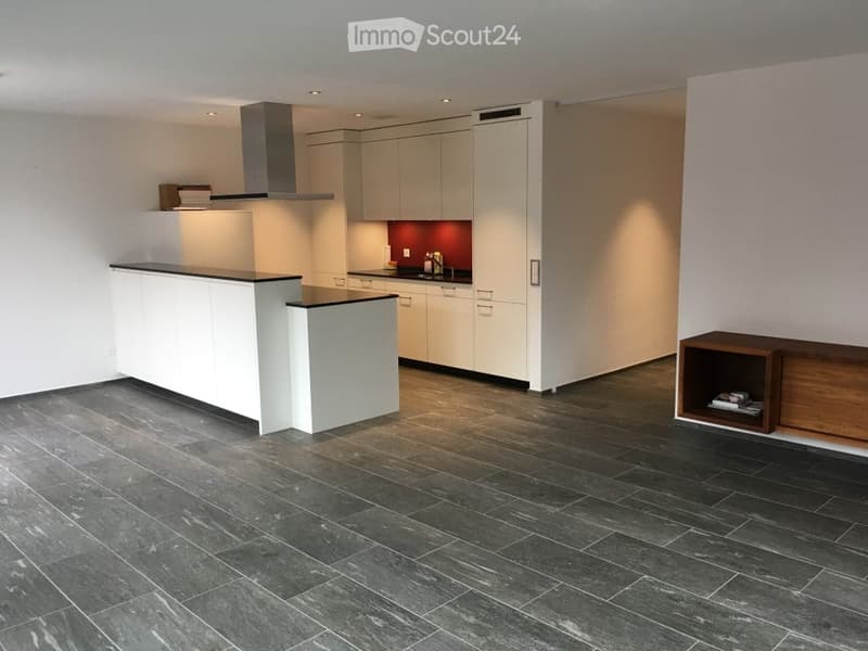 Modern kitchen with white cabinets, a central island, dark tiled floor, and a range hood. A wooden shelf is visible on the right side.