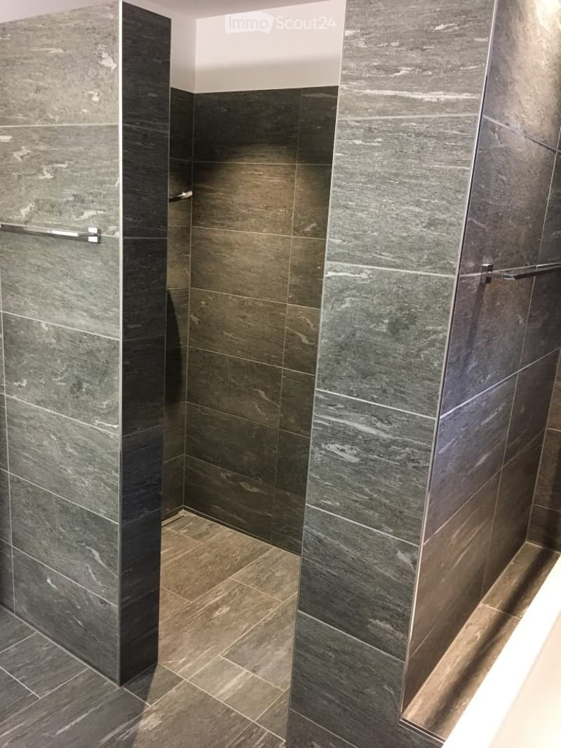 Modern bathroom with dark grey marble tiles on walls and floor, featuring a sleek shower handle.