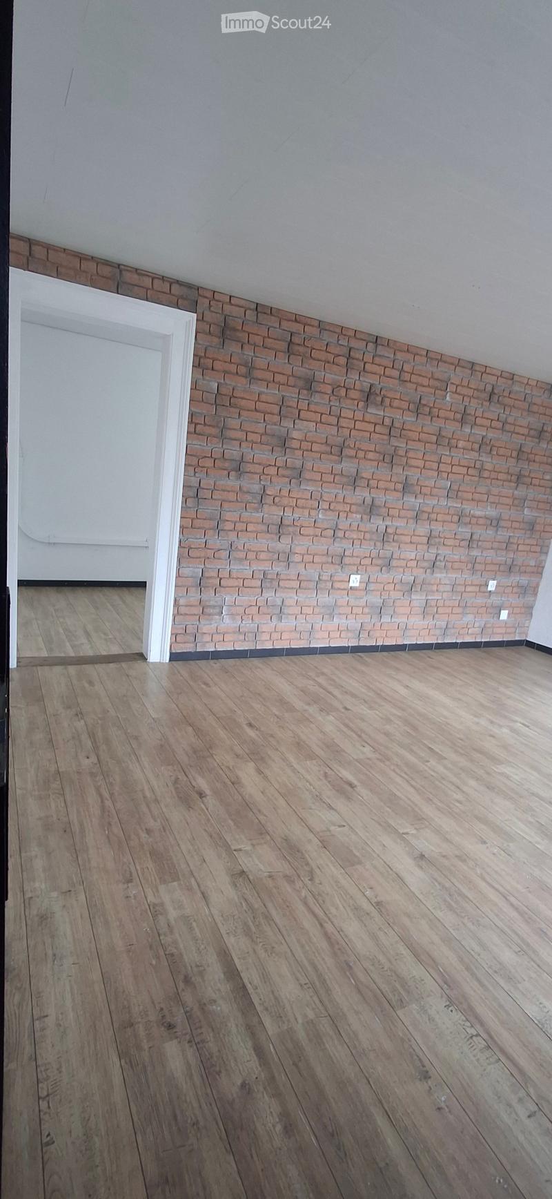 Empty room with wooden flooring and a brick accent wall. The room features a white door frame and visible electrical outlets.