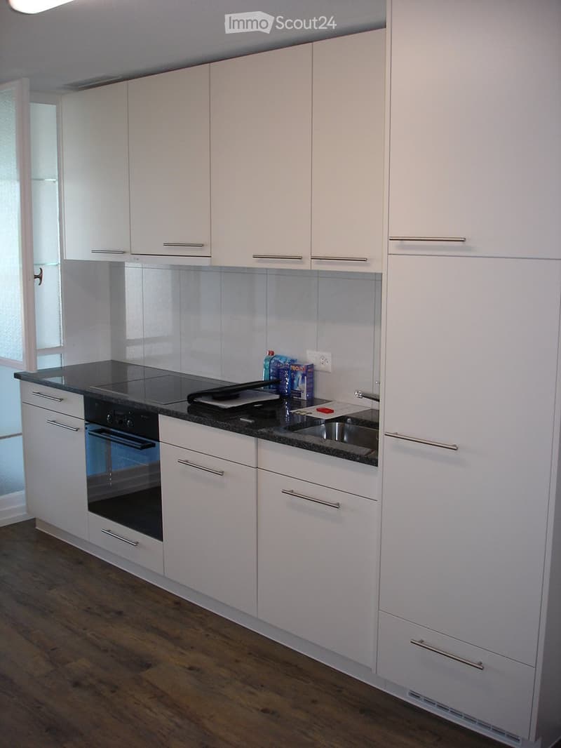Modern kitchen with white cabinets, black countertop, and stainless steel appliances including an oven and sink.