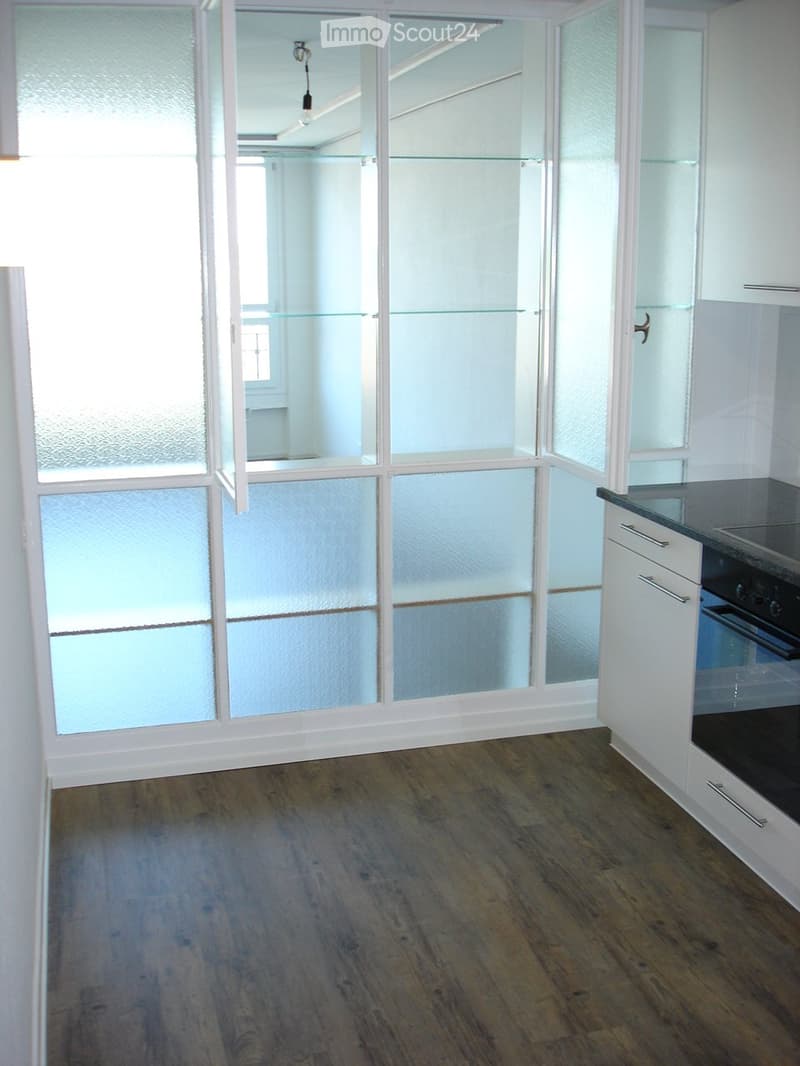 Empty room with wooden flooring, white walls, and large glass partitions. No furniture or appliances are present.