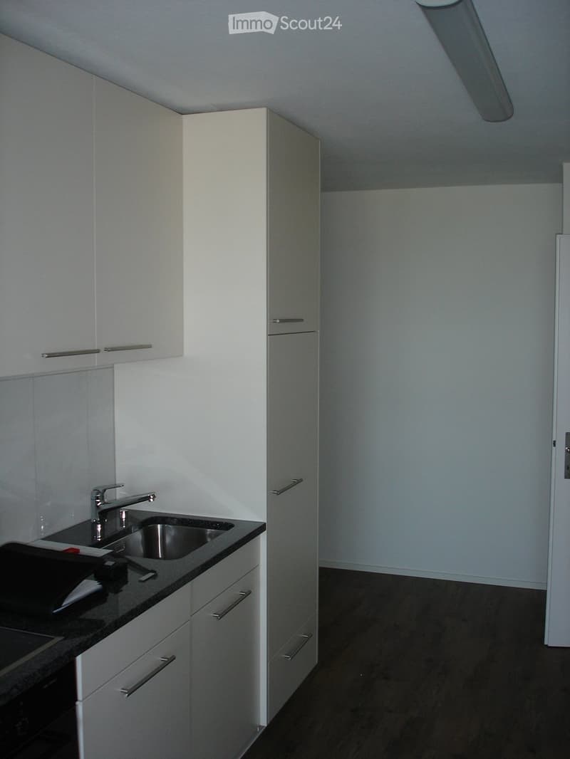 Empty kitchen with white cabinets, black countertop, and stainless steel sink.