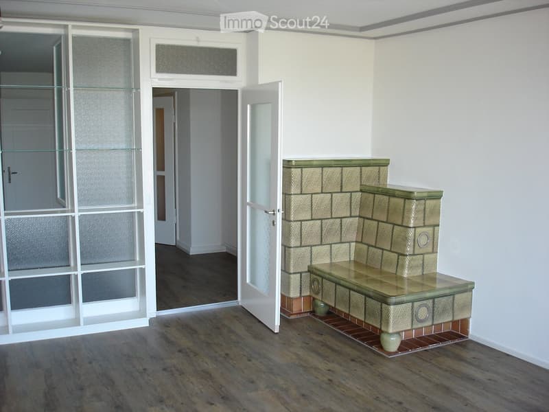Empty room with wooden flooring, white walls, and a fireplace with a bench. There are glass doors leading to another room.