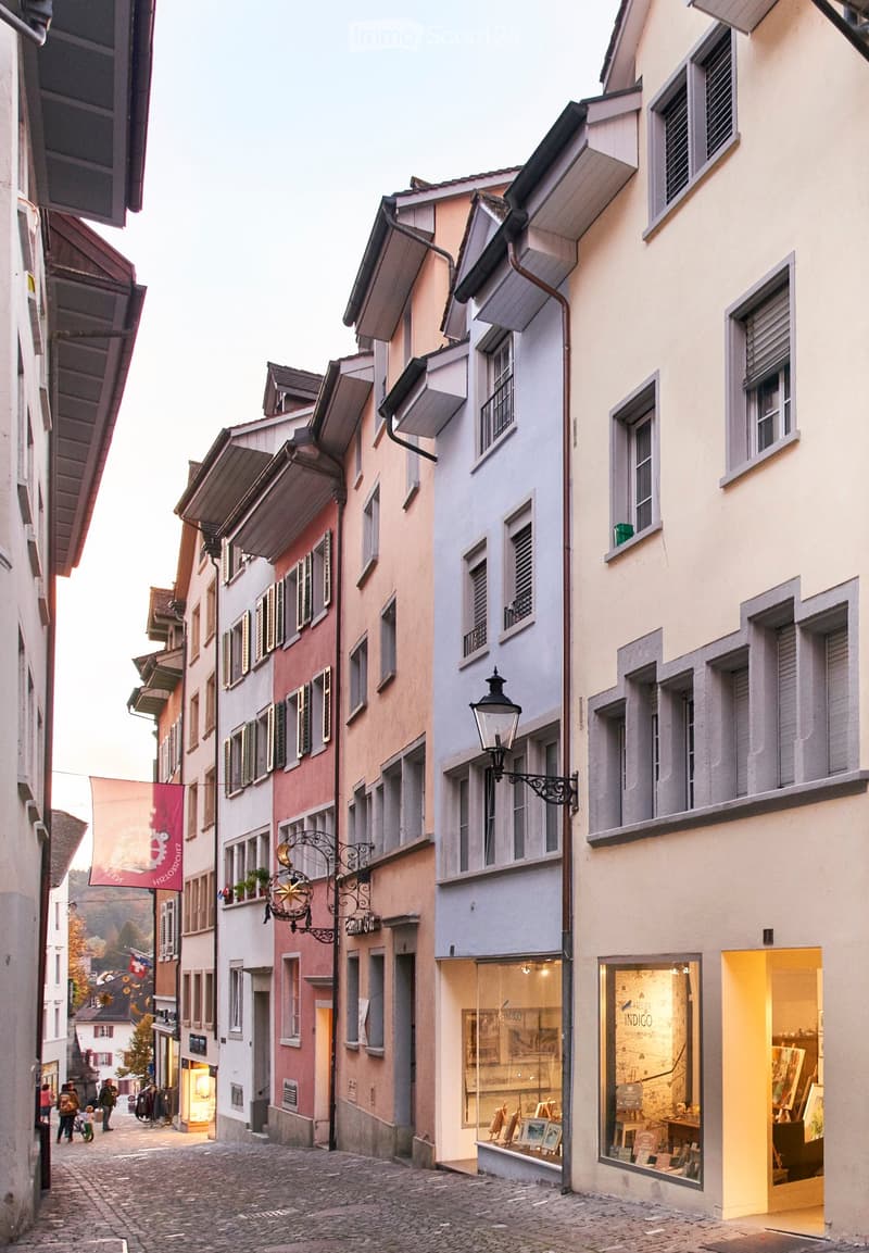 a cobblestone street with several townhouses on both sides, some of which have shops on the ground floor