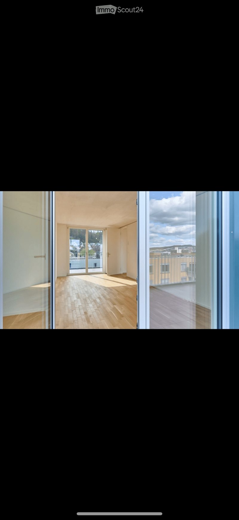 Empty room with wooden flooring, large windows, and sliding glass doors leading to a balcony or terrace.