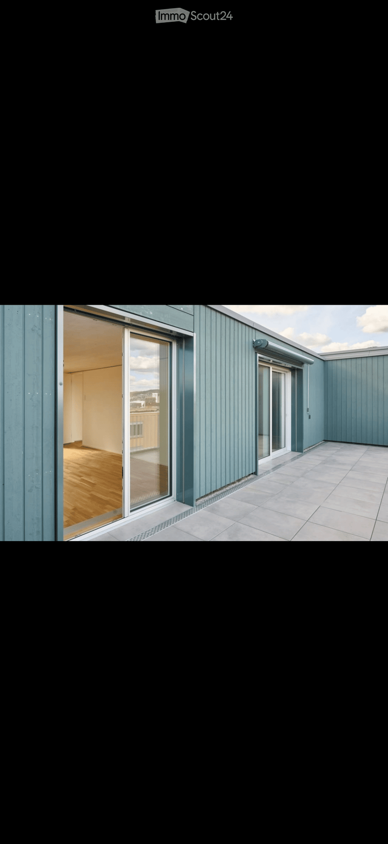 Modern rooftop terrace with light blue paneling, tiled floor, and large glass doors leading to an interior space with wooden flooring.