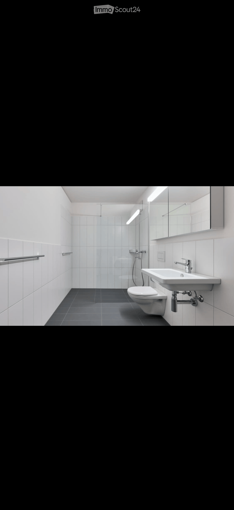 Modern bathroom with white tiles, dark grey floor, sink, toilet, mirror, and shower area.