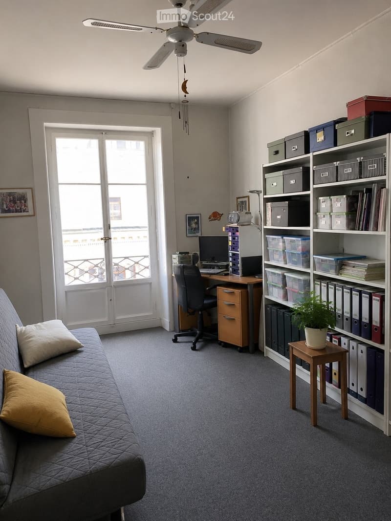A multi-functional room with a sofa, desk, bookshelf, and balcony access. Includes a computer, chair, and storage boxes.