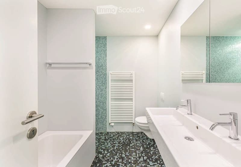 Modern bathroom with white walls, black and white tiled floor, bathtub, toilet, double sink, and a large mirror above the sink.
