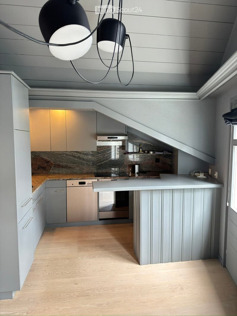 Modern kitchen with light grey cabinets, a central island, and a pendant light fixture. Features a marble backsplash and wooden flooring.