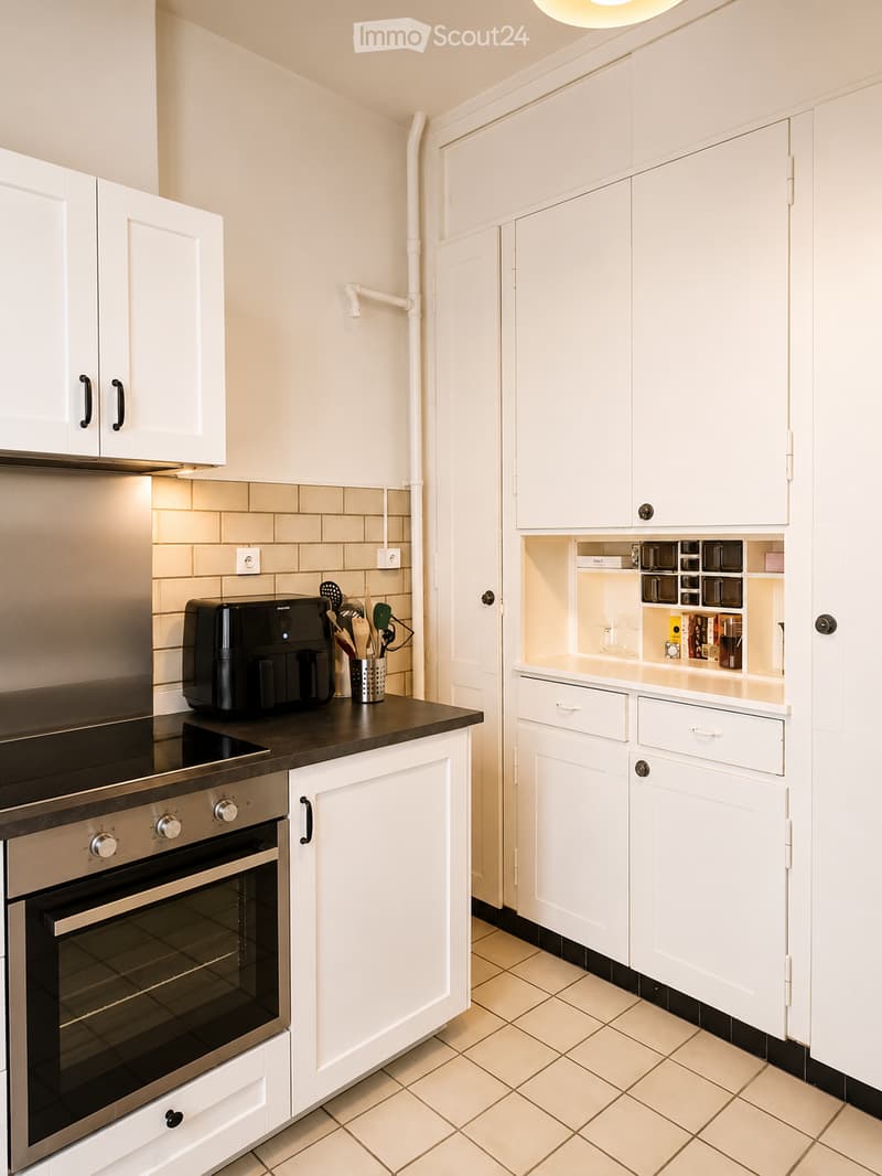 Modern kitchen with white cabinets, stainless steel oven, coffee maker, and tiled backsplash.