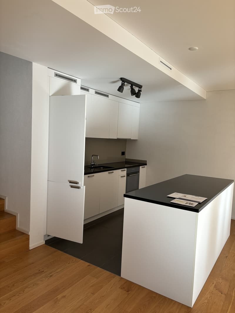 Modern kitchen with white cabinets, black countertops, and a central island. Features include a sink, faucet, and built-in lighting.