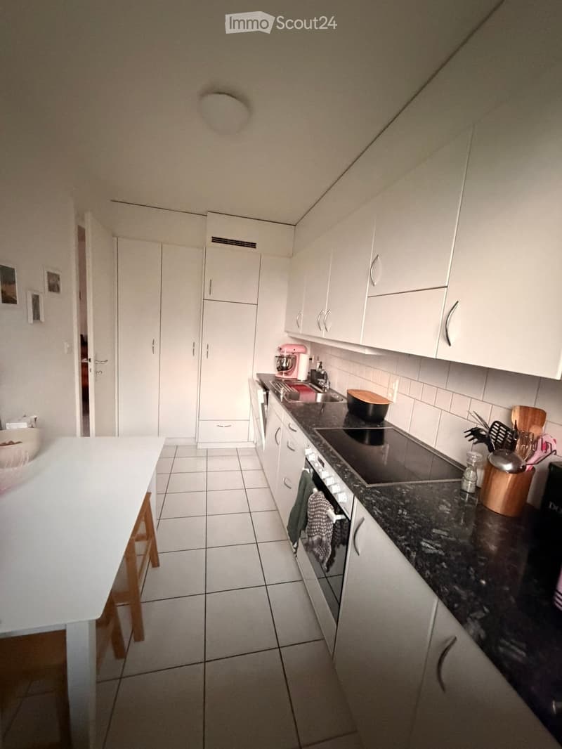 Modern kitchen with white cabinets, dark granite countertops, and stainless steel appliances. Includes a stove, oven, sink, mixer, and various kitchen utensils.