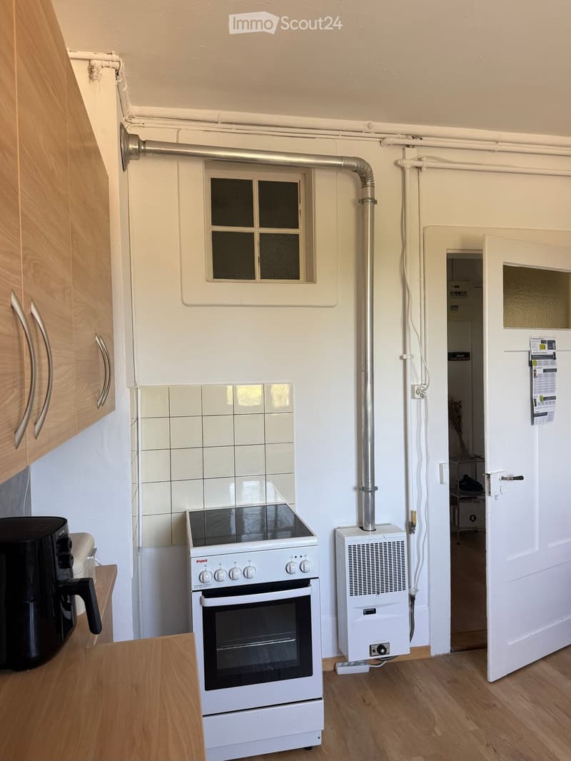Compact kitchen with white tiled backsplash, wooden cabinets, a small oven, and a coffee maker on the counter.