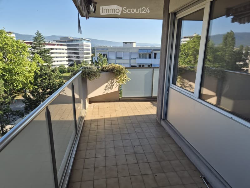 Balcony with tiled floor, glass railing, and view of trees and buildings.