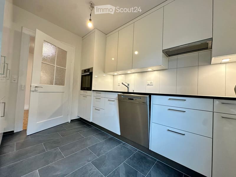 Modern kitchen with white cabinets, stainless steel appliances, dark tiled floor, and a windowed door leading to another room.