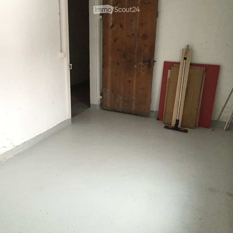 Empty room with a wooden door, a broom, and some stacked wooden planks against the wall.