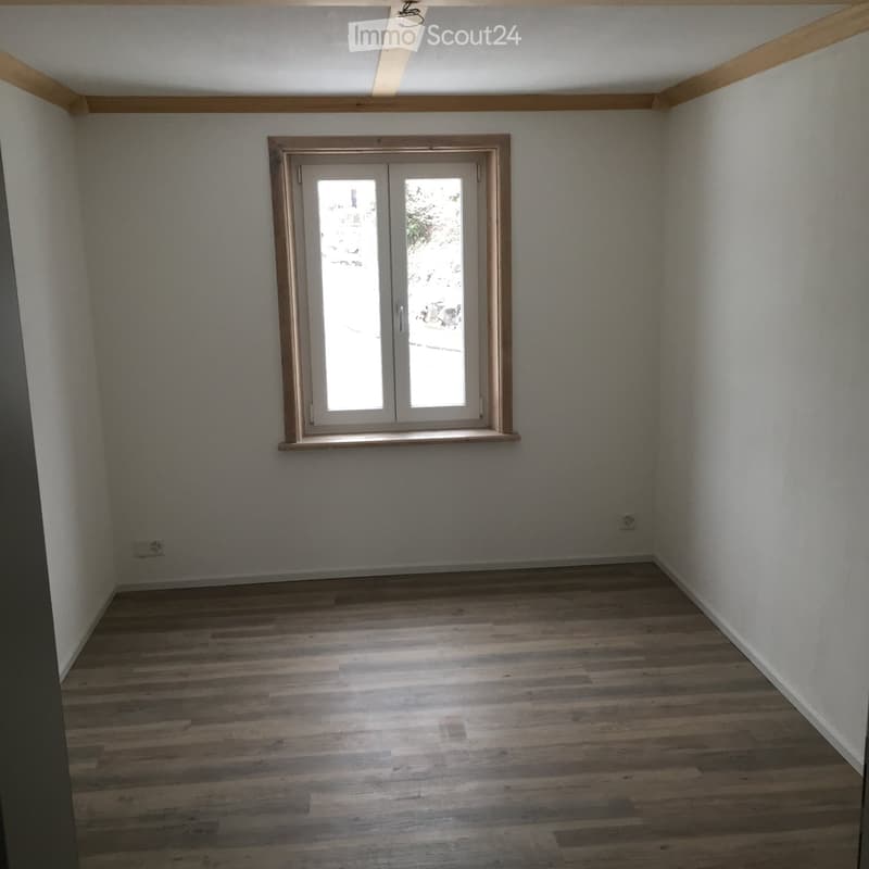 Empty room with wooden flooring, white walls, and a large window with double doors.
