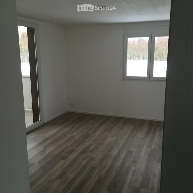 Empty room with wooden flooring, white walls, and large windows with a view of a snowy outdoor area.