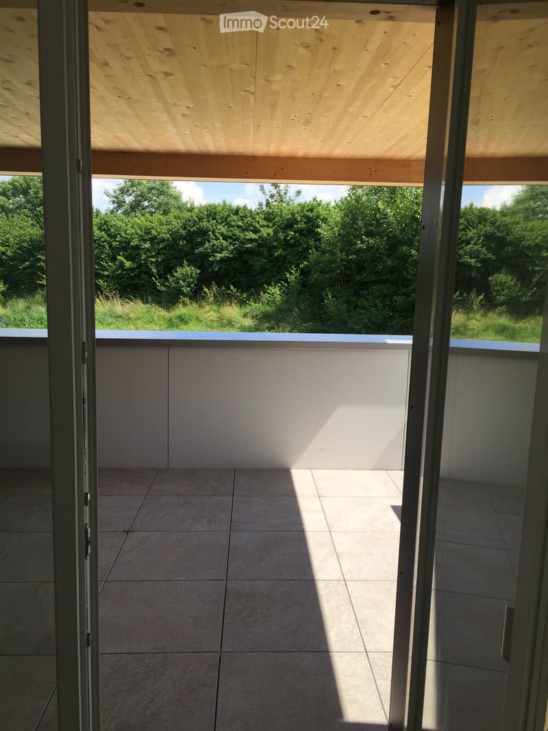 Modern balcony with wooden ceiling, tiled floor, and white railing, offering a view of a green landscape.