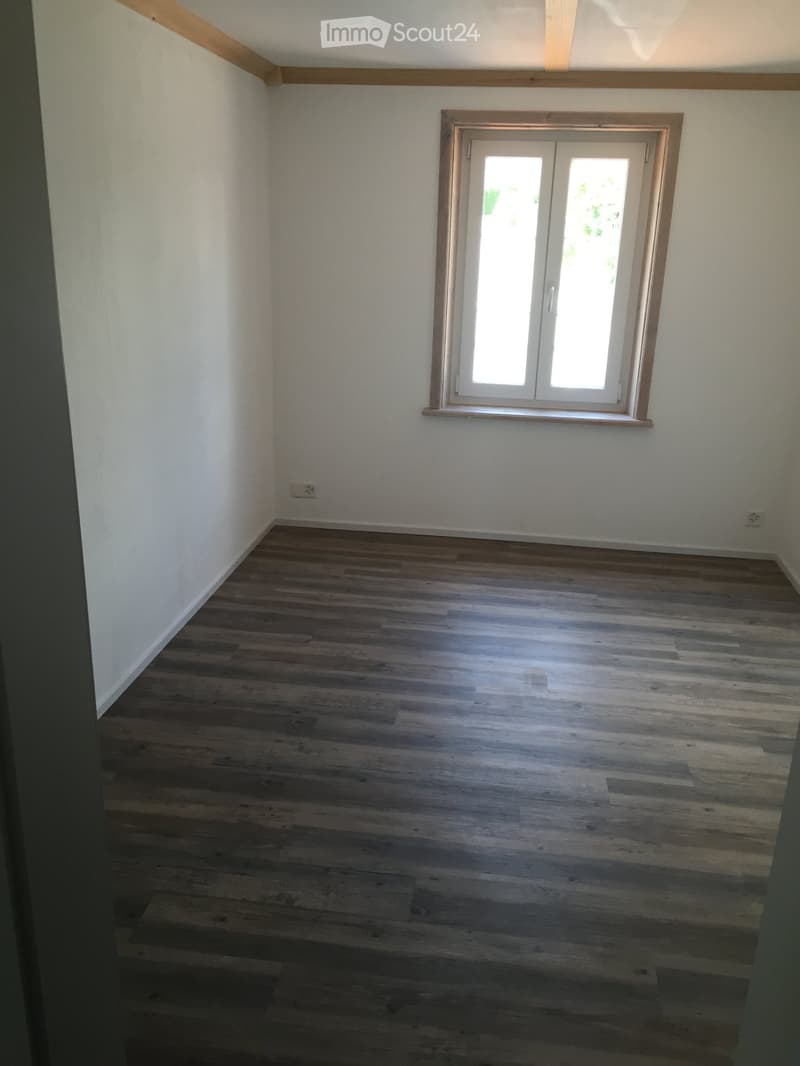 Empty room with wooden flooring and white walls, featuring a single window with white frame and glass panels.