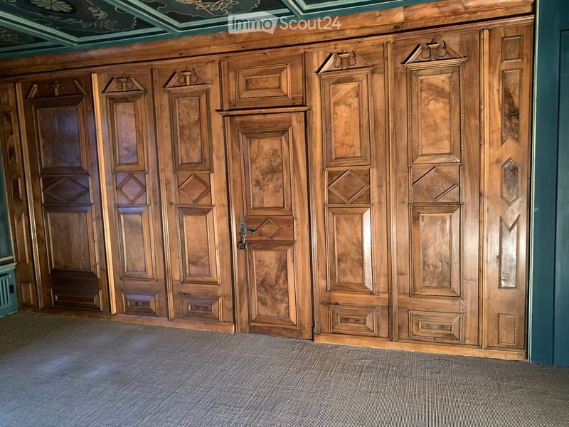 A spacious hallway with ornate wooden paneling and doors, featuring intricate carvings and decorative elements.