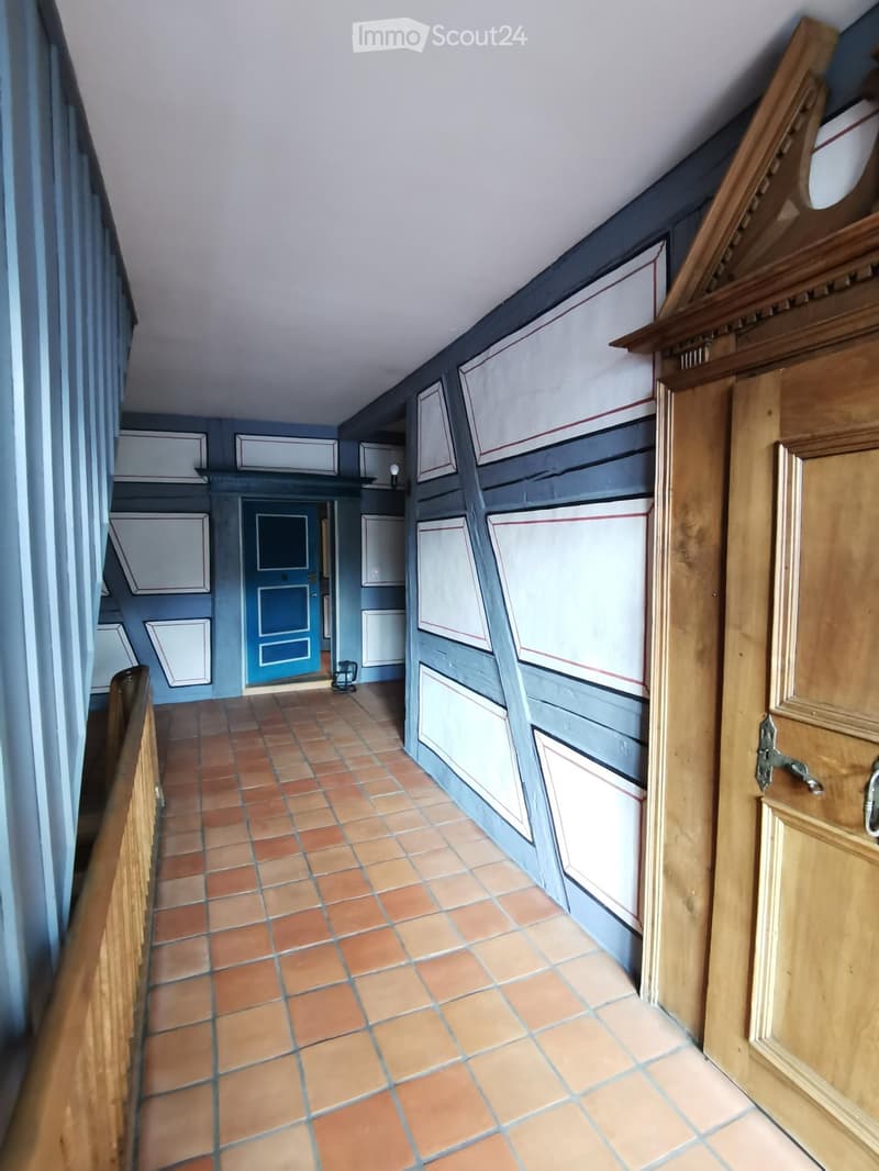 {"visible_features":[],"type":"Hallway","description":"Narrow hallway with terracotta tile flooring, blue and white painted walls, wooden trim and cabinets, and a wooden door frame."}