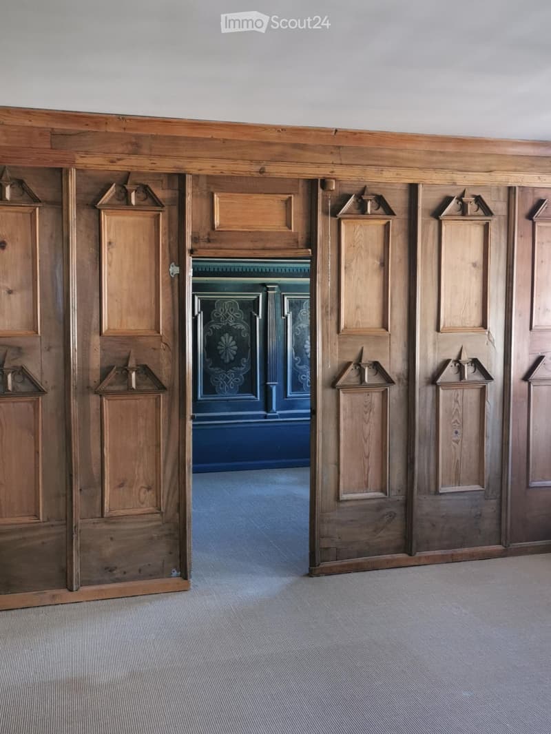 {"visible_features":[],"type":"Interior","description":"The image shows a wooden interior with ornate paneled walls and doors. The doors have decorative elements and the central doorway is painted in a deep blue color. The floor is covered with a gray car