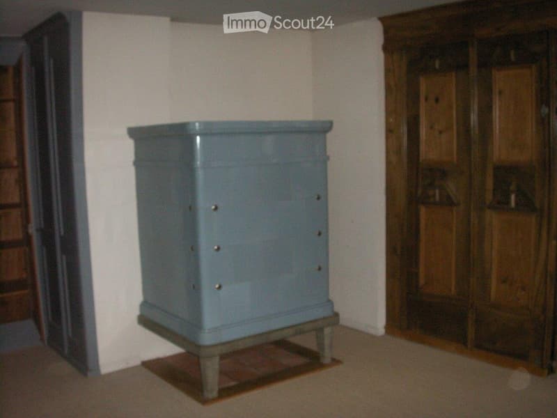 {"visible_features":[],"type":"Room","description":"The image shows a small, square, gray-colored cabinet or storage unit placed on a wooden platform or stand in a room with white walls and a wooden wardrobe or cabinet visible in the background."}