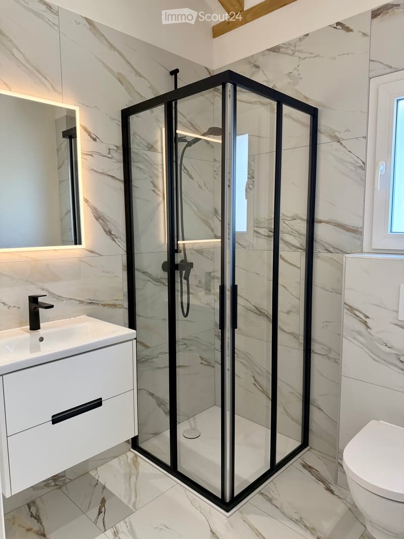 Modern bathroom with marble tiles, glass shower enclosure, white vanity, black faucet, mirror, and white toilet.