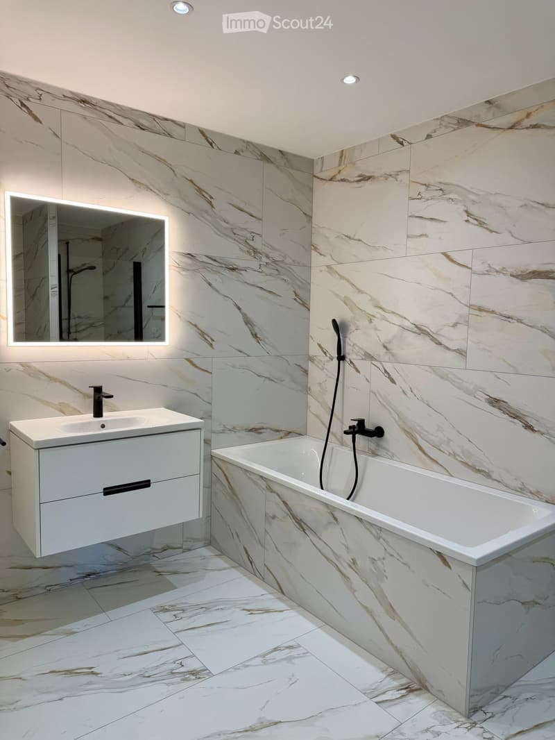 modern bathroom with white marble tiles, white vanity, bathtub, mirror, and black fixtures