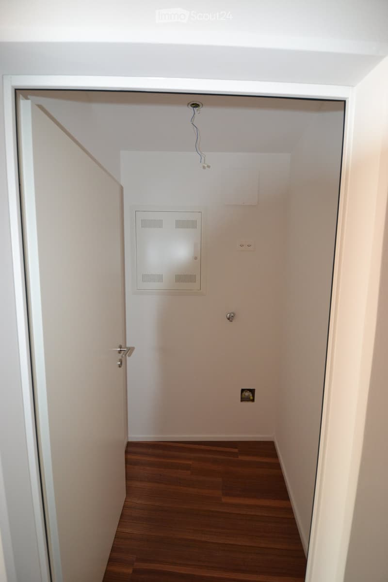 Empty room with wooden flooring, white walls, and a closed door. No furniture or equipment is present.