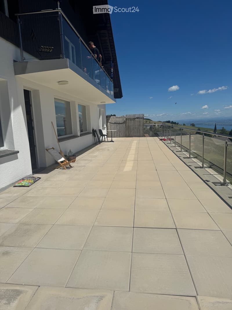 Balcony with tiled floor, glass railing, and outdoor furniture including chairs and a small table.