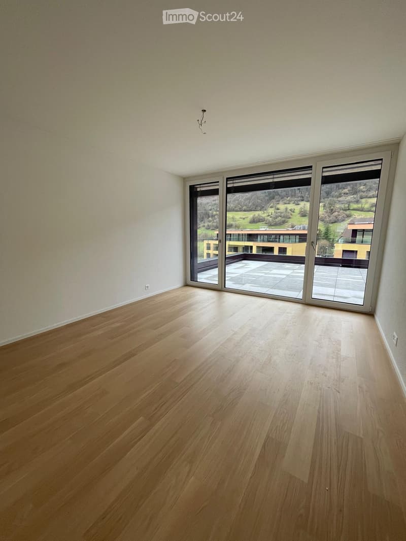 Empty room with wooden flooring, large sliding glass doors leading to a balcony with a scenic view.