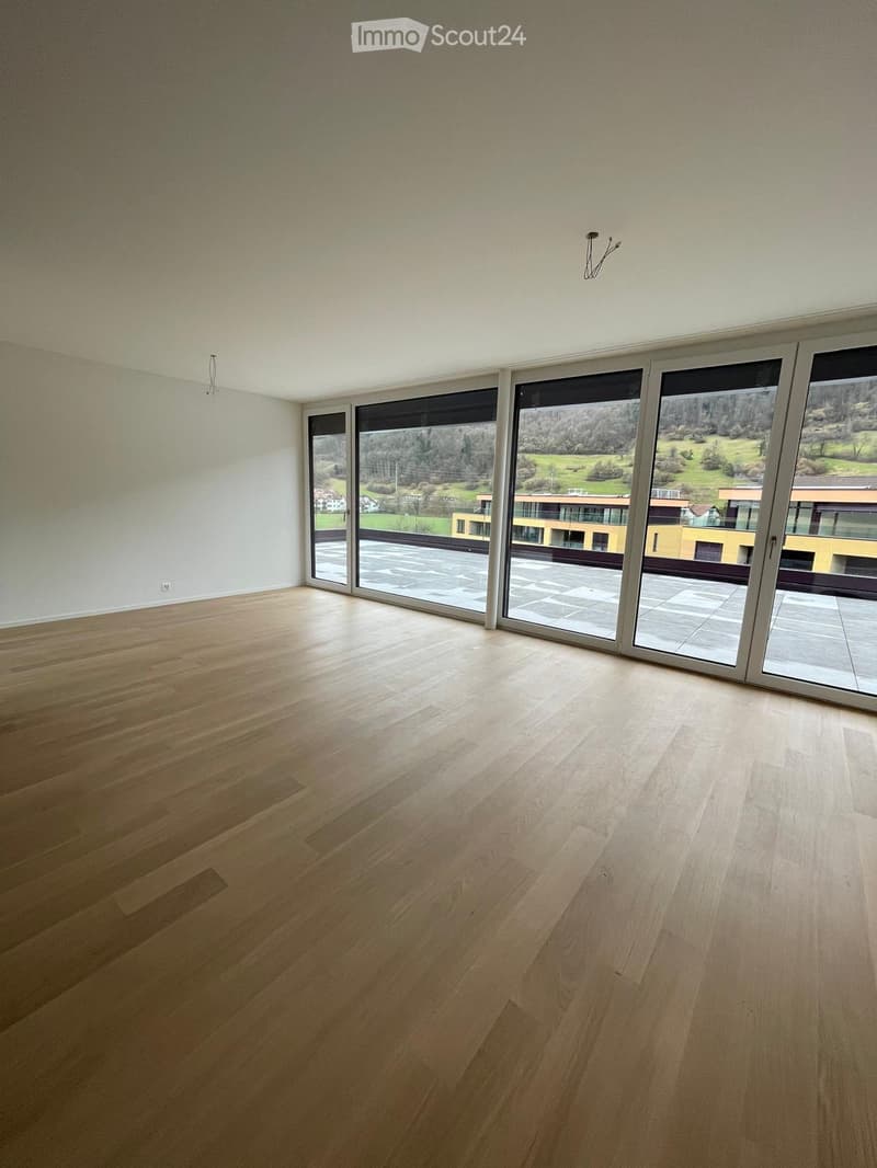 Empty room with light wooden flooring and large glass sliding doors leading to a balcony with a scenic view.
