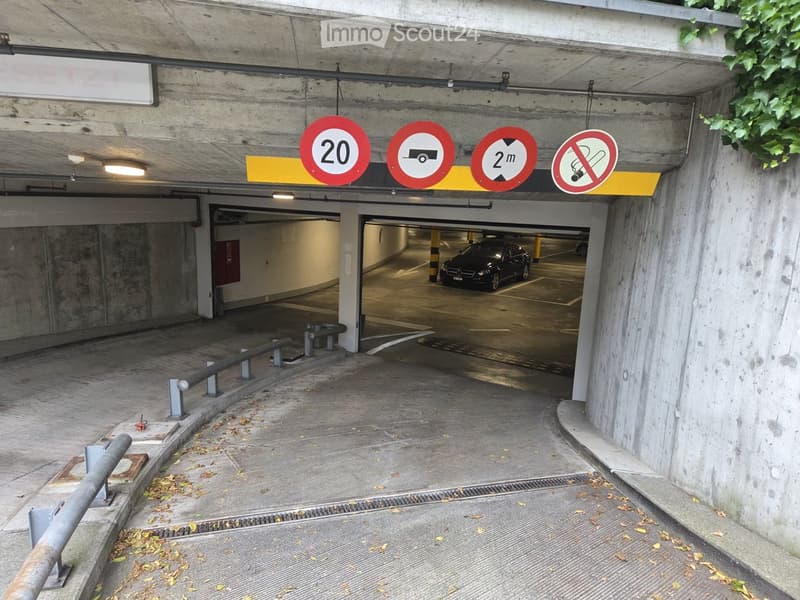 Underground parking area with concrete walls, ceiling, and traffic signs indicating speed limit, no entry, height restriction, and no smoking.