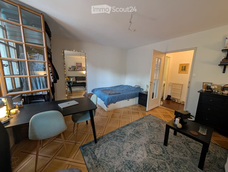 A furnished room with a desk, chair, laptop, bed, nightstand, mirror, sofa, table, shelf, lamp, coffee table, drawer, and picture frame.