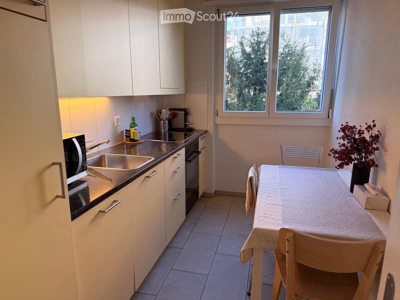 Modern kitchen with white cabinets, stainless steel sink, microwave, and a small dining area with a table and chairs.