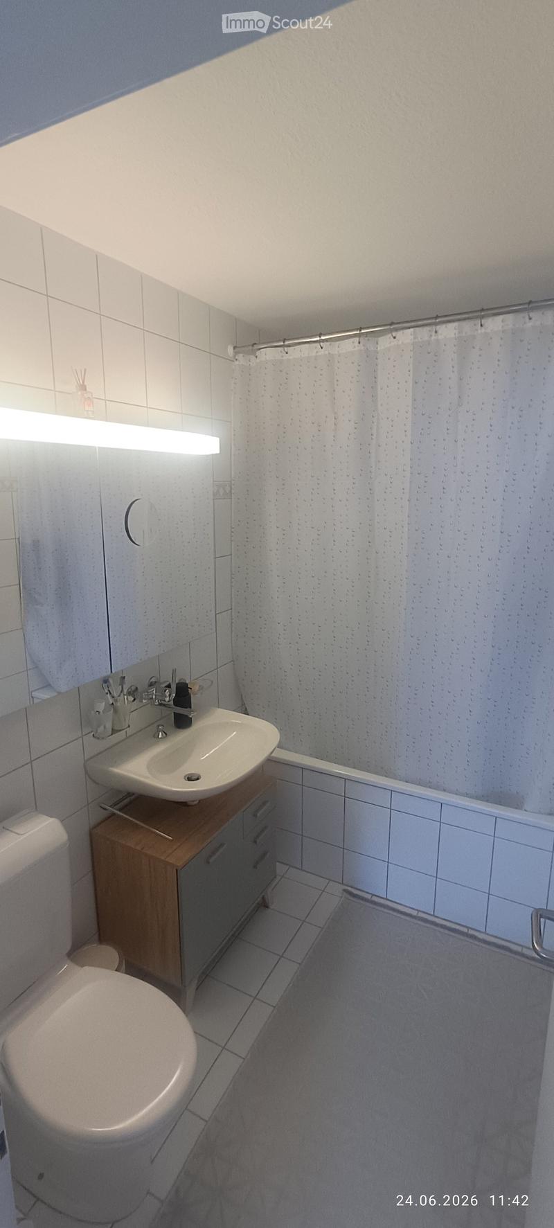 Modern bathroom with white tiles, a toilet, a sink with a wooden cabinet, a mirror, and a shower area with a curtain.