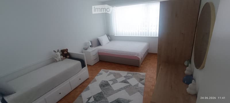 Cozy bedroom with a double bed, nightstand, lamp, sofa bed, and decorative rug. Toys are placed on the sofa bed and floor.