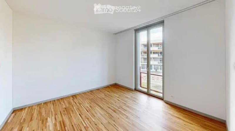 Empty room with wooden flooring and white walls, featuring a large sliding glass door leading to a balcony.